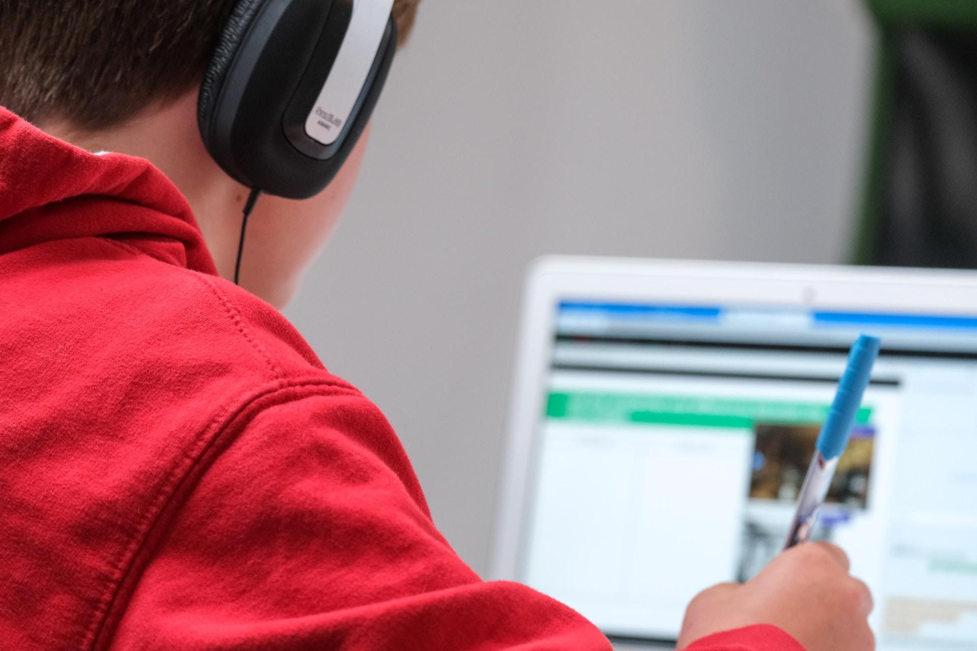 An image of a boy holding a pen and focusing on studying using his laptop.